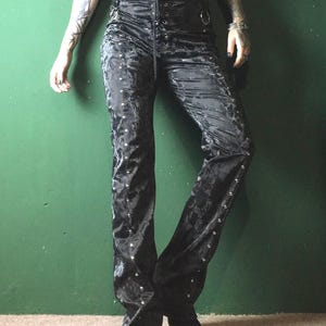 May include: Black velvet pants with a lace-up front and silver stud accents. The pants have a flared leg design and a high waist. The fabric has a subtle pattern. The pants are part of a gothic or alternative fashion style.