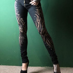 Könnte beinhalten: Schwarze Hose mit Zebra-Muster und silbernen Nieten. Die Hose ist figurbetont und hat einen Reißverschluss.