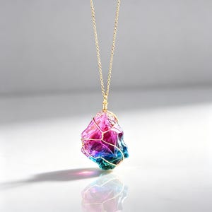 May include: A necklace featuring a raw, multi-colored crystal pendant in shades of pink, purple, and blue, encased in a gold-toned wire wrap. The pendant hangs from a delicate gold-toned chain, creating a vibrant and reflective piece of jewelry.