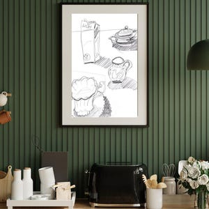 May include: A framed black and white line drawing print featuring a carton, a teapot, a pitcher, and a cup. The artwork is displayed in a thin black frame, showcasing a simple sketch of kitchen items with visible shading and outlines.