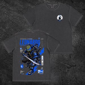 Peut inclure: Un t-shirt gris anthracite à manches courtes avec un petit motif circulaire sur la poitrine et une grande illustration détaillée au dos. Le motif arrière représente une tortue au masque bleu tenant une épée avec le texte LEONARDO.