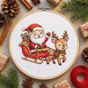 Op de afbeelding: Een ronde houten borduurring met een kruissteekontwerp van de Kerstman in een rode slee vol cadeautjes, getrokken door een bruin rendier met een groen-rood gestreepte sjaal, alles op een witte stoffen achtergrond.