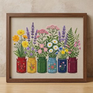 May include: A framed cross-stitch embroidery featuring six colourful metal milk cans arranged in a row, each holding a different variety of wildflowers including yellow cosmos, purple lavender, pink yarrow, white daisies, and green ferns.