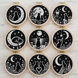Peut inclure: Neuf tambours à broder circulaires présentant des motifs au point de croix en noir et blanc de chats dans diverses scènes nocturnes, incluant des chats sur des croissants de lune, sous des pleines lunes, sur des toits et dans des jardins fleuris.