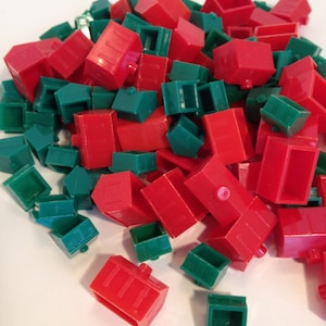 May include: A pile of red and green plastic houses, commonly used in board games. The red houses have a rectangular shape with a chimney, while the green houses are smaller and square. The houses are scattered on a white surface.