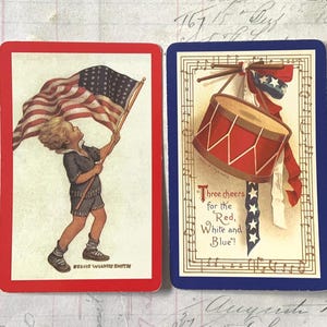 May include: Two vintage playing cards with patriotic themes. One card features a child waving an American flag, framed in red. The other card, framed in blue, shows a drum and text that reads "Three cheers for the Red, White and Blue!"