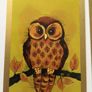 Op de afbeelding: Een bruine uil met gele ogen zit op een tak met bruine bladeren. De uil heeft een patroon van bruine driehoeken op zijn lichaam.