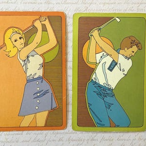 May include: Two vintage golf-themed playing cards. One card features a woman in a white top and blue skirt, the other a man in a white shirt and blue pants. Both cards have a yellow-orange border and a green background.