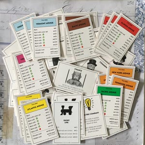 May include: A collection of Monopoly game cards, including property deeds, chance cards, and community chest cards. The cards are white with black text and illustrations. Some of the cards feature property names like Vermont Avenue, Baltic Avenue, and Illinois Avenue. Other cards feature Chance and Community Chest.
