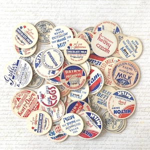 May include: A collection of vintage milk bottle caps with various designs and text. The caps feature red, white, and blue color schemes, with phrases like "Chocolate Milk," "Pasteurized Milk," and "Dairy Products."