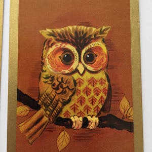 Op de afbeelding: Een bruine en gele uil met oranje ogen zit op een tak met bruine bladeren. De uil heeft een patroon op zijn veren.