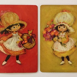 May include: Two vintage playing cards featuring illustrations of a girl. One card shows a girl in a dress and hat carrying a basket of fruit against a red background. The other card depicts a girl holding flowers on a yellow background.