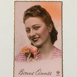 May include: A vintage postcard featuring a woman with brown hair and a pink and white striped shirt. She is holding a bouquet of pink flowers and smiling. The postcard has a gold border and the text "Bonne Année" written in cursive.