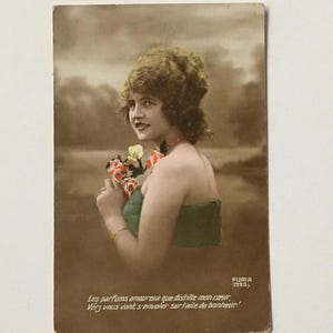 May include: A vintage postcard featuring a woman with curly hair holding a bouquet of pink and white flowers. The postcard is sepia toned and has the text "FURIA 1990" and a French quote in the bottom corner.