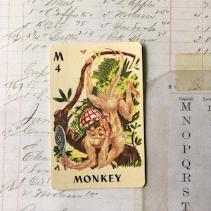 May include: Vintage playing card featuring a cartoon monkey hanging from a tree branch. The monkey is wearing a hat and holding a mirror. The card has the letter "M" and the number "4" at the top, with the word "MONKEY" at the bottom.