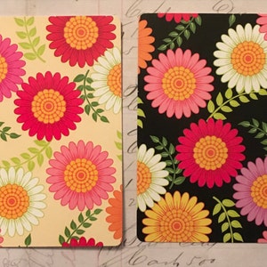 May include: Two cards with a floral pattern. One card has a yellow background with pink, red, and white flowers. The other card has a black background with pink, red, white, and purple flowers.