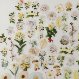 以下が含まれることがあります： 白い紙に様々な花のステッカーが貼られています。ステッカーには、白、黄、ピンクの花、葉、キノコが描かれています。