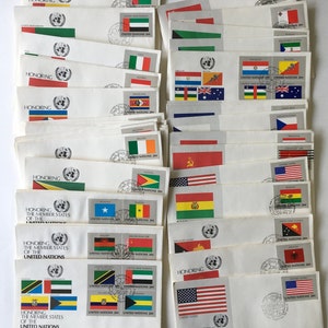 May include: A collection of envelopes with stamps featuring flags of different countries. The stamps are part of a series honoring the member states of the United Nations. The envelopes are dated 1984 and include the text "First Day of Issue".