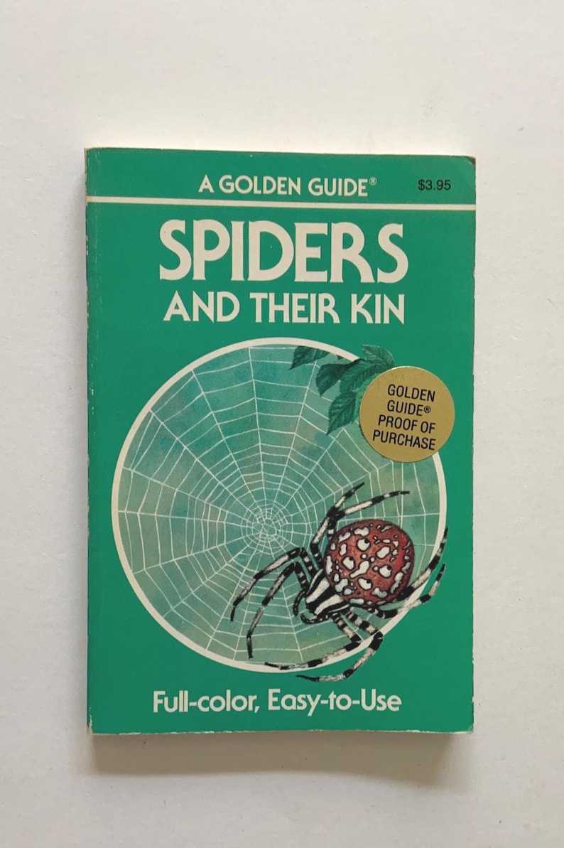 May include: A paperback book titled A GOLDEN GUIDE SPIDERS AND THEIR KIN with a green cover. The cover features a white spider web illustration, a red and white patterned spider, and a gold circular sticker that reads GOLDEN GUIDE PROOF OF PURCHASE.