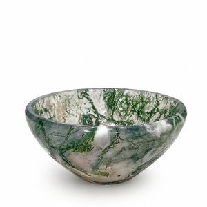 Può includere: Una ciotola in agata muschiata lucida caratterizzata da una base bianco latte traslucida con intricate inclusioni verdi ramificate che ricordano motivi di fogliame naturale su tutta la superficie curva e liscia del recipiente in pietra.