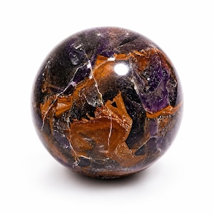 May include: A polished spherical stone featuring a complex pattern of deep purple, dark black, and warm brown mineral inclusions. The surface is smooth and reflective, showcasing natural crystalline textures and veins throughout the sphere.