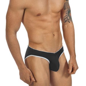 May include: A black brief with a V-shaped waistband and white trim along the leg openings and waist. The garment features a contoured front pouch design and is constructed from a solid-coloured fabric with contrasting white piping details.