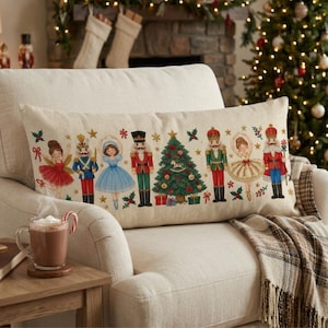 May include: A rectangular lumbar pillow with a beige fabric base featuring a colorful print of nutcracker figures, ballerinas, and a decorated Christmas tree. The design includes small gold stars, red bows, and green holly leaves scattered across the surface.