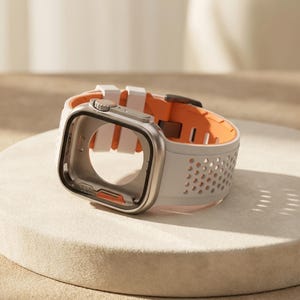 May include: A silver-toned smartwatch protective case with a white silicone band featuring a perforated design. The band has a bright orange interior lining and a metallic buckle. The case frame is rectangular with rounded corners and a side crown.