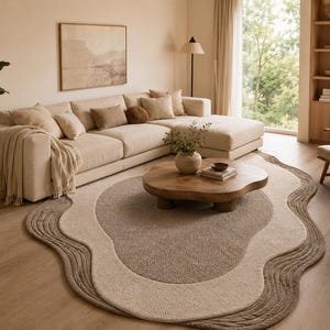 Op de afbeelding: Een vloerkleed met een onregelmatige, organische vorm en gelaagde, golvende randen in tinten cr&egrave;me, beige en bruin. Het kleed heeft een getextureerd, getuft oppervlak met een centraal donkerbruin ovaal gedeelte omringd door ringen.