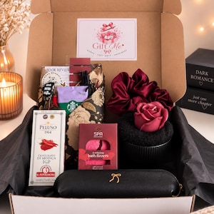 Puede incluir: Una caja de regalo que contiene una tableta de chocolate Peluso 1964 con chile, una caja de bombas de baño Spa Exclusives, un estuche negro con un lazo dorado, un coletero de satén rojo oscuro, una vela con forma de rosa y una ficha de lectura.