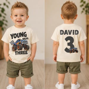 May include: A cream-colored t-shirt featuring a blue monster truck graphic with the text Young Wild & Three on the front and the name David with the number 3 and a smaller monster truck graphic on the back, paired with olive green shorts.