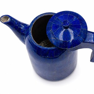 Peut inclure: Une théière bleu profond présentant une surface de style mosaïque composée de nombreuses petites pièces de lapis-lazuli incrustées. La théière comprend un couvercle circulaire assorti avec un bouton central, une anse courbée et un bec verseur.