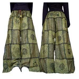 May include: Wide-leg pants in olive green featuring a patchwork design with black sun and spiral motifs. The garment has a drawstring waist with brown ties and visible stitching between the rectangular fabric panels, shown from front and back.