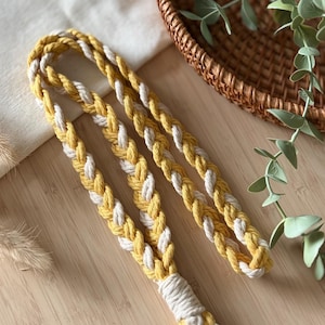 May include: A braided lanyard crafted from mustard yellow and off-white cotton cord. The design features a repeating plait pattern secured at the base with a tightly wrapped white cord knot, finished with a silver-toned metal split ring and clasp.