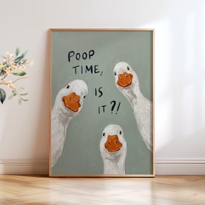 May include: A framed wall art print featuring three white geese with orange beaks against a sage green background. The text "POOP TIME, IS IT?!" is written in black, hand-drawn style lettering between the geese, which have a textured paint appearance.