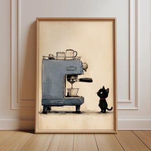 May include: A framed wall art print featuring a blue espresso machine with a small white cup underneath. A small black cat with a red collar stands to the right, looking up at the machine. The background is a light beige, and the style is illustrative.