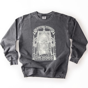 May include: A charcoal gray crewneck sweatshirt featuring a white graphic print of a gothic cathedral structure. The text reads ARCHITECTURA SYSTEMATIS at the top, MICROSERVICES and API GATEWAY on the pillars, and CORE DATABASE at the base.