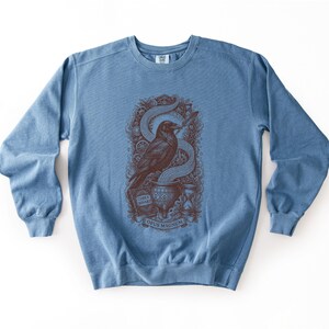 Denim blue cyberpunk apparel sweatshirt displaying a dark red Opus Magnum raven graphic on the chest.