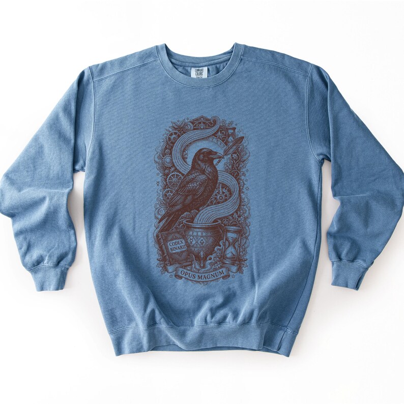 Denim blue cyberpunk apparel sweatshirt displaying a dark red Opus Magnum raven graphic on the chest.