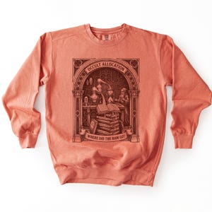 Op de afbeelding: Een koraalkleurig sweatshirt met ronde hals en een donkerbruine grafische print van een alchemist in een laboratorium. Het ontwerp bevat een boogframe, een open boek, gestapelde boeken en de tekst Occult Allocation en Where Did The Ram Go?