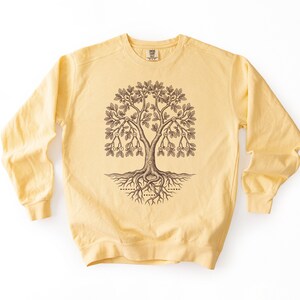 May include: A pale yellow crewneck sweatshirt featuring a dark brown graphic of a tree with intricate roots and branches. The tree design includes small circles containing numbers arranged in a branching pattern, with Morse code symbols below the roots.