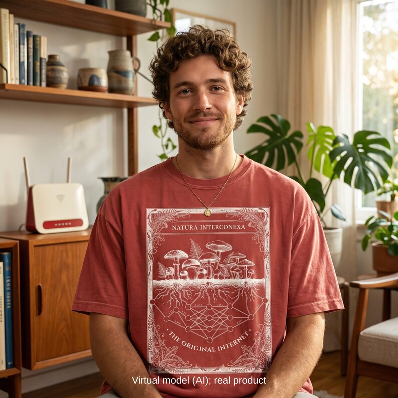 Male virtual model wearing a terracotta red vintage t-shirt with a white "Natura Interconexa" mushroom mycelium network and math nodes graphic. Cozy indoor plant and bookshelf background.
