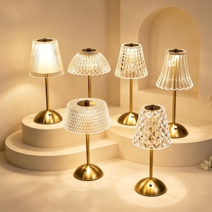 Könnte beinhalten: Eine Sammlung von sechs Tischlampen mit goldfarbenen runden Sockeln und schlanken Stielen. Jede Lampe hat einen individuellen Lampenschirm aus klarem Acryl mit unterschiedlichen Texturen, darunter vertikale Rillen, Rautenmuster und gewellte Ränder.