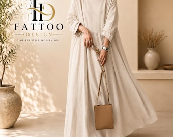 May include: A floor-length, long-sleeved beige dress with a round neckline and a loose, flowing silhouette. The garment is paired with a small, rectangular tan handbag featuring a braided strap. The text FATTOO DESIGN TIMELESS STYLE, MODERN YOU is visible.