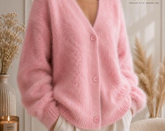 May include: A fuzzy, light pink V-neck cardigan with long sleeves and three matching buttons down the front. The knit fabric has a soft, brushed texture. The logo FATTOO DESIGN TIMELESS STYLE. MODERN YOU. is visible in the upper right corner.