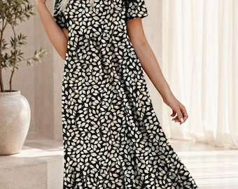 May include: A midi-length dress featuring a black background with a repeating pattern of white and beige leaves. The dress has short sleeves, a V-neckline, and a tiered skirt design. The logo FATTOO DESIGN TIMELESS STYLE MODERN YOU is visible.