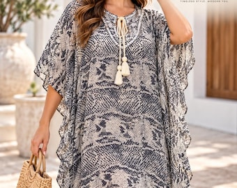 May include: A loose-fitting kaftan dress featuring a grey and beige snakeskin print, wide flutter sleeves, and a round neckline with a white embroidered trim and cream-coloured tassel ties. The garment has a high-low hemline and a relaxed silhouette.