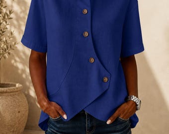 May include: A royal blue short-sleeved shirt featuring a classic collar and an asymmetrical front button placket with four visible brown buttons. The garment has a textured fabric finish and a layered, overlapping hemline design.