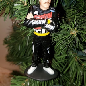 May include: A Christmas ornament featuring a race car driver wearing a white hat and a black and red racing suit with the word "Castrol" printed on it.