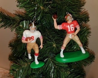 Op de afbeelding: Twee vintage kerstversieringen van San Francisco 49ers footballspelers. De versiering links is van een speler die een wit shirt draagt met nummer 8. De versiering rechts is van een speler die een rood shirt draagt met nummer 16.